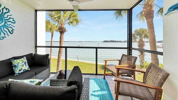 A balcony with a view of the sea, a ceiling fan, and a sofa with cushions. - Water view condo with shared pool, panoramic balcony views, and WIFI (Marco Island)