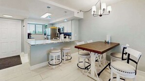 Una cocina moderna con una isla central, taburetes blancos para bar y una mesa de comedor con sillas.