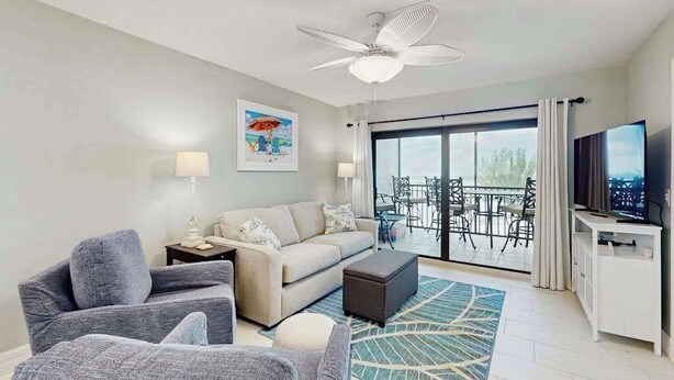 Una sala de estar moderna con sofá, sillones, televisor y un balcón con mobiliario exterior.