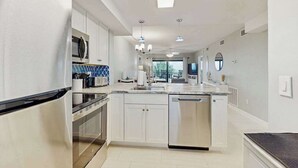 Una cocina moderna con armarios blancos, electrodomésticos de acero inoxidable, una isla central e iluminación colgante.