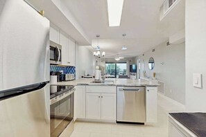 A modern kitchen with white cabinetry, stainless steel appliances, a central island, and pendant lighting. - Beachfront condo with screened balcony, community pool, and internet (Fort Myers Beach)
