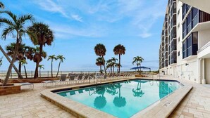 Una piscina con sillones de descanso, palmeras y un edificio con balcones.