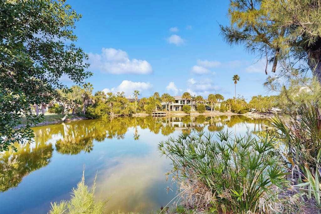 A house by a calm lake with surrounding greenery and a clear sky.