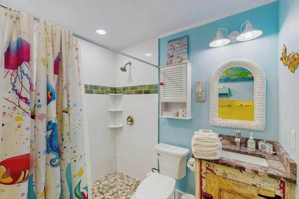 A bathroom with a shower, toilet, sink, and a mirror.
