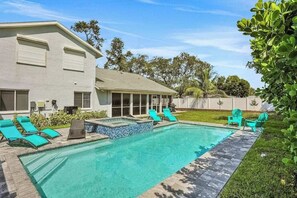 A swimming pool with lounge chairs, a covered patio, and a house with large windows. - 6BR Resort-Style Compound | Pool & Spa | Sleeps 12 | 2 Homes in One | Near Beach (Bonita Springs)