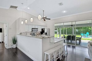 A modern kitchen with a central island, pendant lights, and a view to an outdoor patio. - 6BR Resort-Style Compound | Pool & Spa | Sleeps 12 | 2 Homes in One | Near Beach (Bonita Springs)