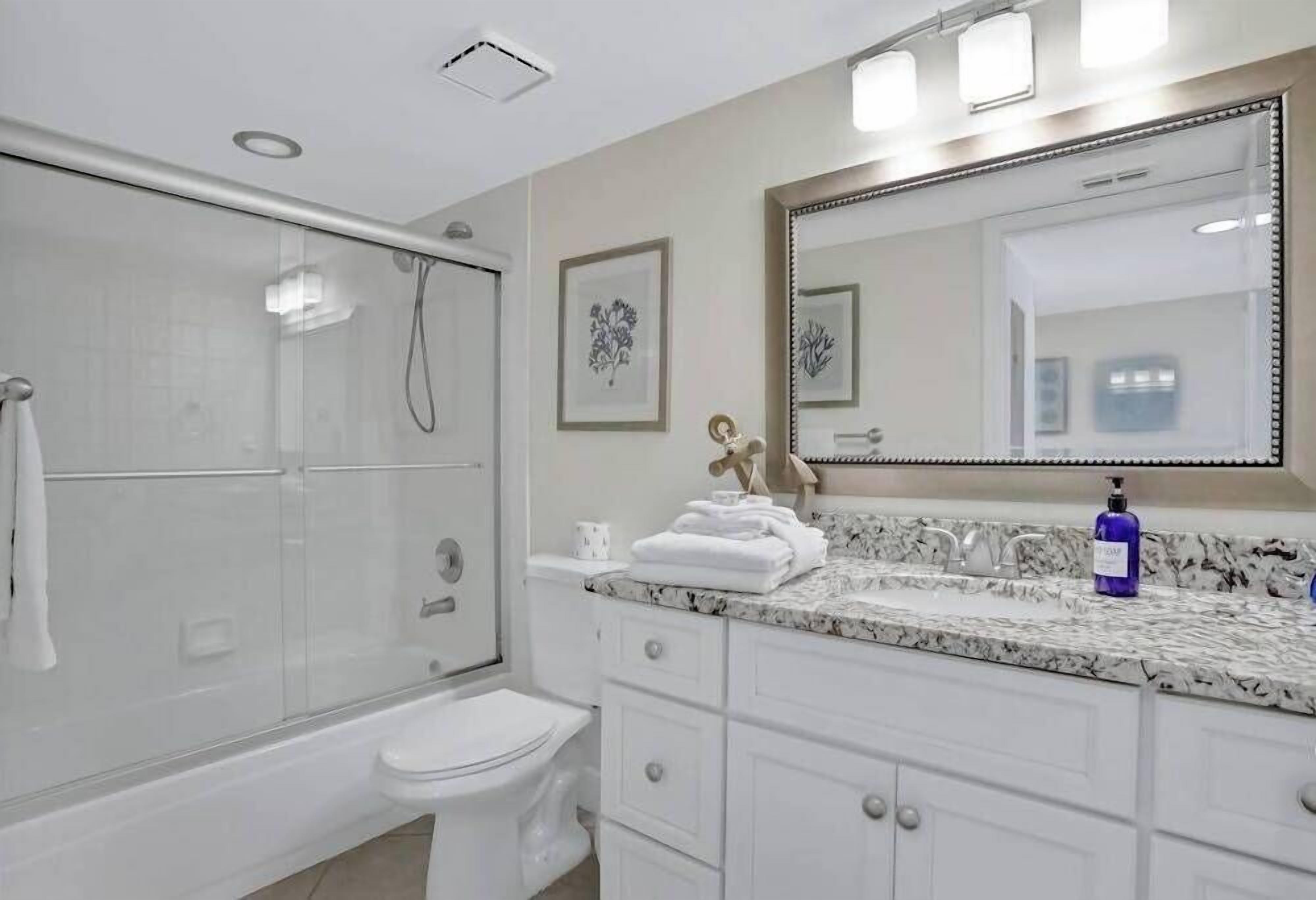 A modern bathroom with a glass-enclosed shower, a white toilet, a marble sink, and a large mirror.