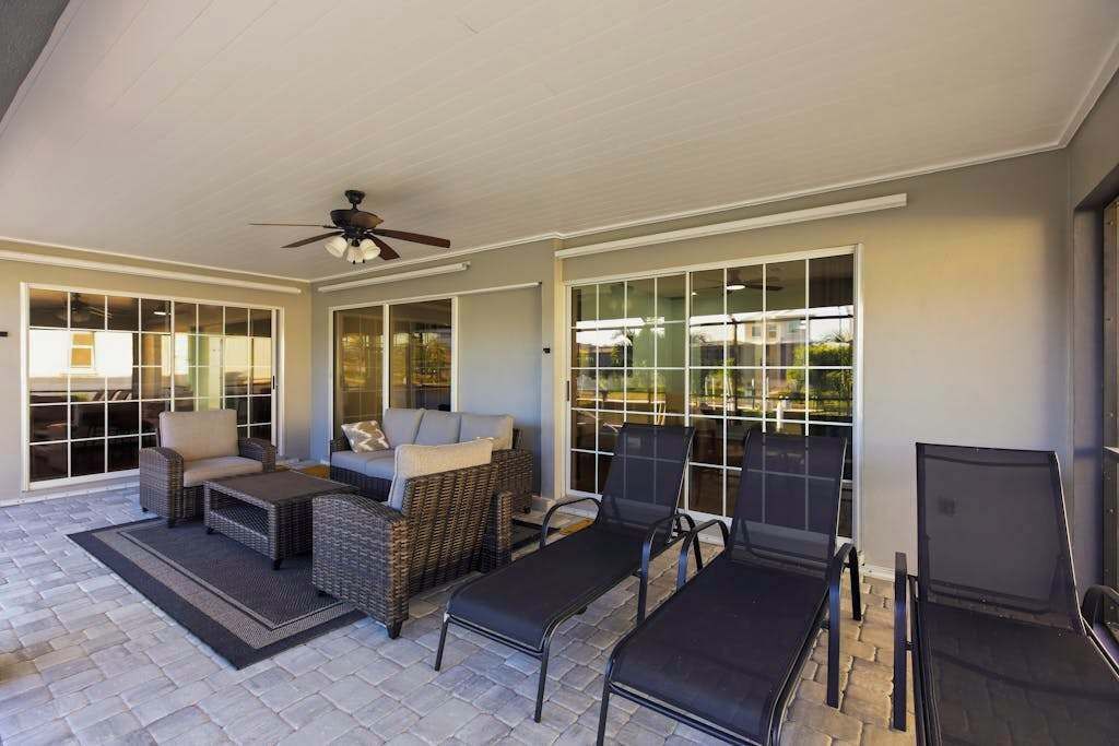 A covered patio area with wicker furniture, a ceiling fan, and large glass doors leading to a view.