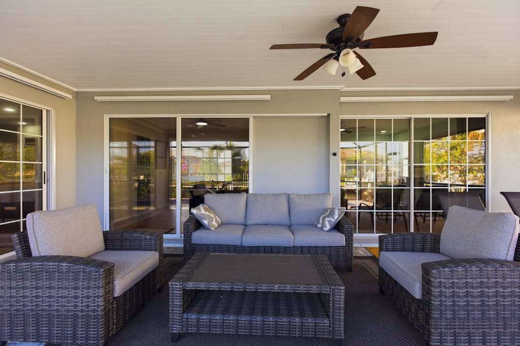 An outdoor seating area with wicker furniture, a ceiling fan, and large windows.