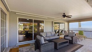 Une terrasse couverte, meublée de mobilier en osier, dotée d’un ventilateur de plafond et offrant une vue sur l’océan.