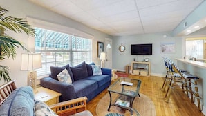 A living room with a sofa, coffee table, and chairs, a television, and a window with a view of buildings. - Dog-friendly duplex with outdoor living - walk to beach & downtown (Venice)