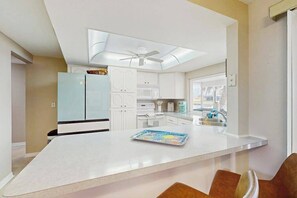 A modern kitchen with white cabinets, a blue refrigerator, a ceiling fan, and a dining area with brown chairs. - Riverfront Relaxation. The Perfect Escape for Adventure, Comfort, and Fun. (Port Charlotte)