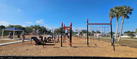 Un parque infantil con diversas estructuras de juego, una zona de estar cubierta y un cielo despejado.