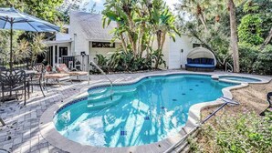 A swimming pool with a tiled edge, surrounded by a patio area with chairs and a covered seating area. - Chic Home With Private Pool, Hot Tub & Covered Lanai - Snowbirds Welcome (Sanibel)