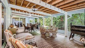 An open-plan living area with a wooden ceiling, large windows, wicker furniture, and a piano. - Chic Home With Private Pool, Hot Tub & Covered Lanai - Snowbirds Welcome (Sanibel)