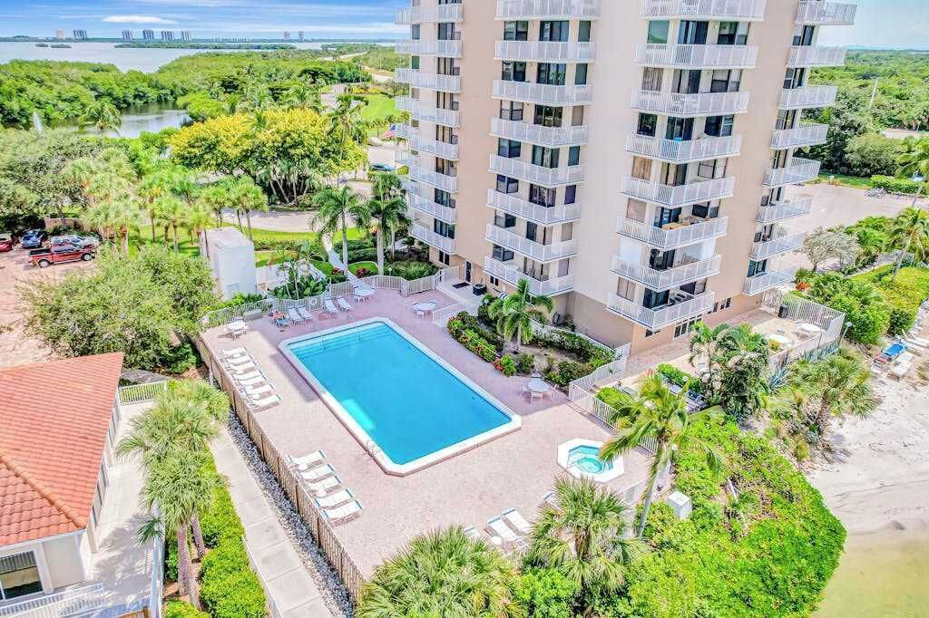 A high-rise building with a swimming pool and outdoor seating, surrounded by greenery and a view of the water.