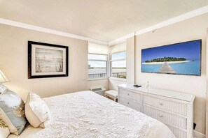 A bedroom with a bed, a dresser, a framed picture, and a TV. - Waterfront condo with private beach area, pool, hot tub, grills, & balcony (Fort Myers)