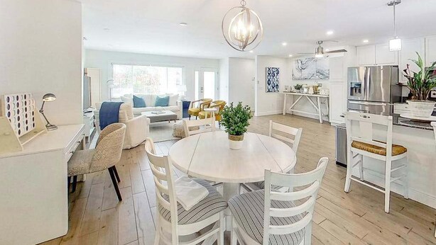 Eine moderne Küche mit weißen Schränken, ein Essbereich mit rundem Tisch und Stühlen sowie ein Wohnzimmer mit Sofa und Sesseln.