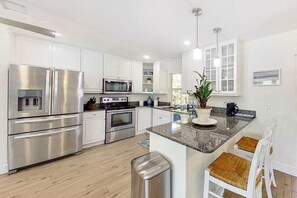 A modern kitchen with stainless steel appliances, white cabinetry, and a central island with seating. - Spacious & beautiful home with fast WiFi, central AC, patio, and W/D (Naples)