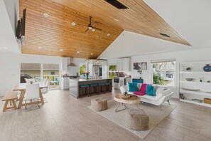 A modern kitchen with a central island, a dining area with a wooden table and chairs, a living room with a white sofa and colorful cushions, and a ceiling with wooden beams and recessed lighting. - Stunning waterfront home, contemporary, family friendly, close to Gulf with pool (Marco Island)