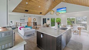 Amplia sala de estar con isla de cocina, techo de madera y ventanas grandes.