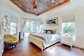 Ein Schlafzimmer mit Holzbalkendecke, einem Bett, einem Sessel, einem Nachttisch und einem Fenster mit Vorhängen.