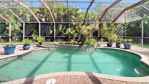 Un espace piscine doté d’une structure en verre, entouré de plantes en pot et offrant une vue dégagée sur l’extérieur.