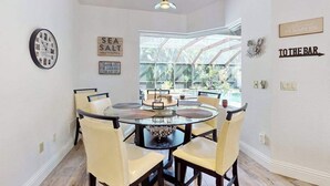 Un espace repas comprenant une table ronde en verre, des chaises, une horloge et des éléments de décoration murale.