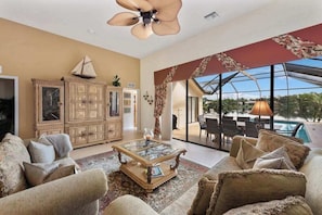 A spacious living room with a large glass door leading to a pool area, a ceiling fan, and a traditional cabinet. - Lakeside paradise with private pool, tennis courts, and more (Naples)