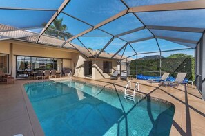 A pool with a glass enclosure, lounge chairs, and a patio area. - Lakeside paradise with private pool, tennis courts, and more (Naples)