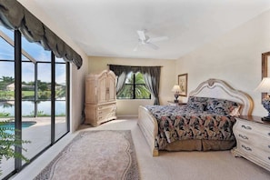 A bedroom with a bed, a dresser, a nightstand, a ceiling fan, a window with curtains, and a view of a pool. - Lakeside paradise with private pool, tennis courts, and more (Naples)