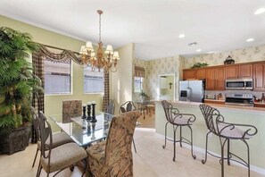 A dining area with a glass table, chairs, and a chandelier. - Lakeside paradise with private pool, tennis courts, and more (Naples)