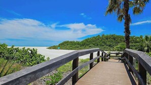 A wooden boardwalk leading to a beach with a clear sky. - Waterfront, gulf view condo by beach with pool, dock & balcony (Marco Island)