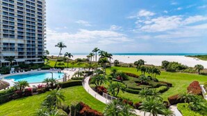 A resort with a swimming pool, palm trees, and a beach view. - Waterfront, gulf view condo by beach with pool, dock & balcony (Marco Island)