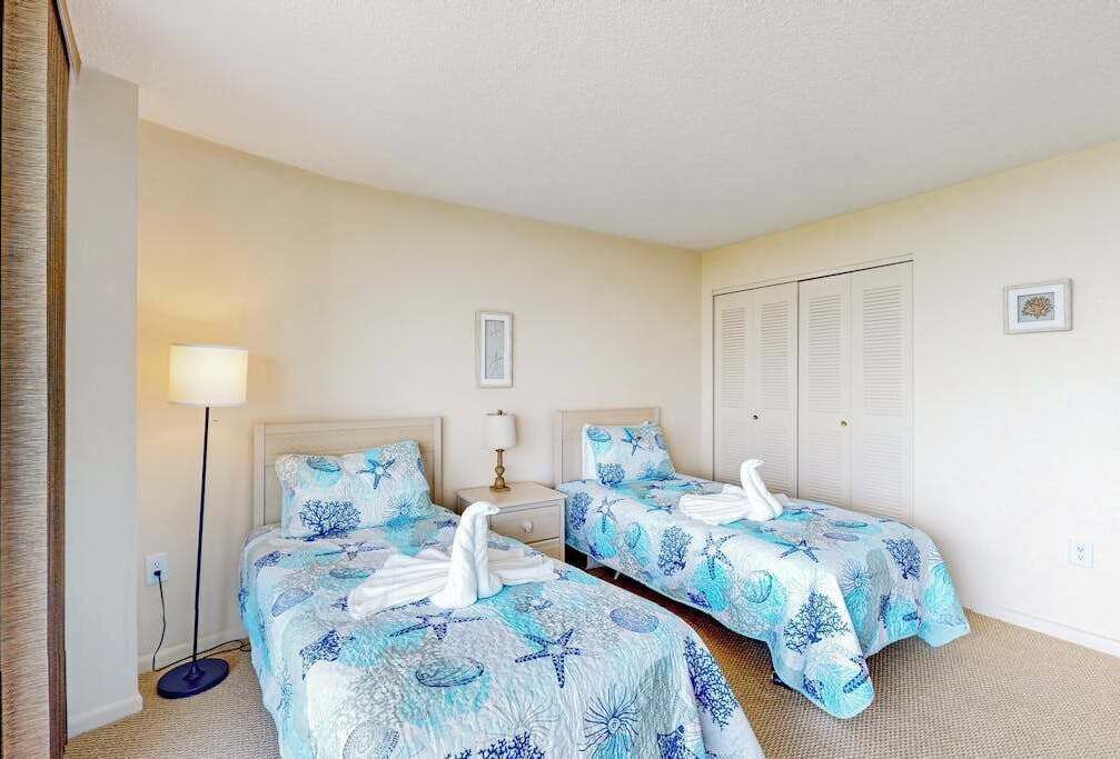 A hotel room with two beds, a nightstand, a lamp, a closet, and a picture on the wall.