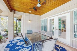 A covered patio with a glass table and chairs, wooden ceiling, and large windows. - Exquisite home near Marco Island Beach with saltwater pool, patio & dogs (Marco Island)