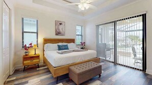 A bedroom with a bed, a nightstand, a bench, a ceiling fan, and a large sliding glass door. - Canal-front home with private pool, pool spa, dock, boat access, grill, gym, W/D (Marco Island)