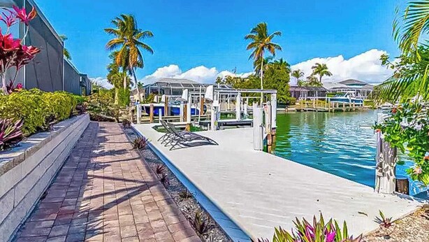 A waterfront hotel with a pool, palm trees, and a covered area with lounge chairs. - Canal-front home with private pool, pool spa, dock, boat access, grill, gym, W/D (Marco Island)