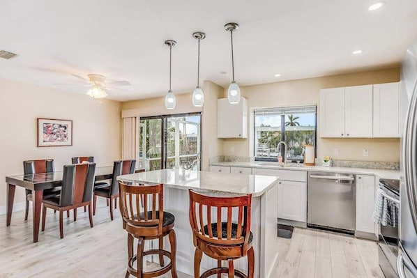 Una cocina moderna con una isla central, armarios blancos y un comedor con sillas de madera.