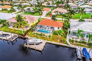 A residential area with a house featuring a swimming pool, a dock with a boat, and a red location marker.