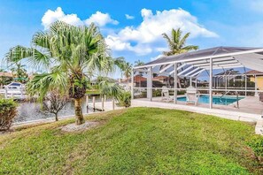 A covered outdoor area with a pool, palm trees, and a clear sky.