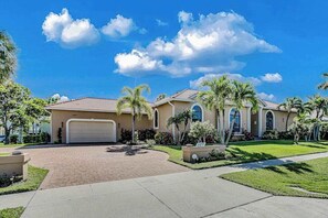 A residential house with a garage, palm trees, and a clear blue sky. - Canal-front home with fast WiFi, pool, & lanai - near beach (Marco Island)