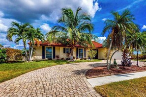 A house with a red roof, palm trees, and a brick pathway. - Waterfront Home with Private Dock & Enclosed Lanai - Near Residence Beach (Marco Island)
