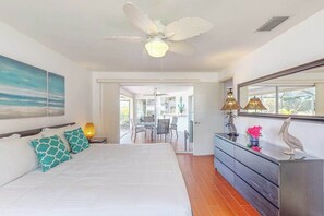 Un dormitorio con cama, ventilador de techo, cómoda, espejo y vista al balcón.