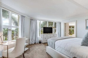 Een slaapkamer met een bed, bureau, televisie en grote ramen.