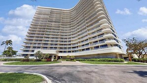 Un hotel de varios pisos con fachada curva, múltiples balcones y un patio ajardinado.