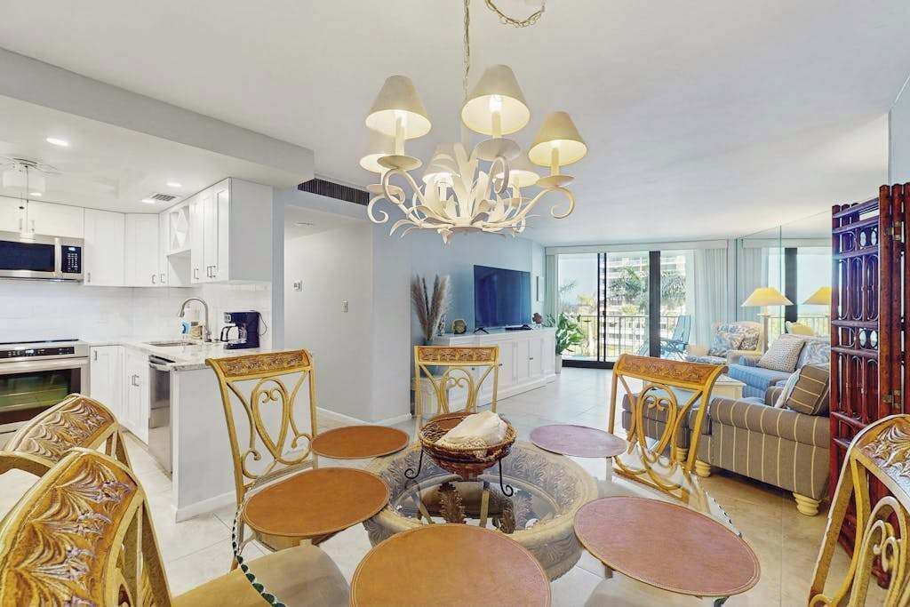 Une cuisine moderne avec des meubles blancs, un îlot central et un coin repas agrémenté de chaises décoratives et d’un lustre.