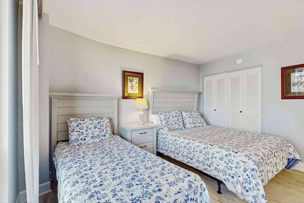 A room with two beds, a nightstand, a lamp, and a wardrobe.