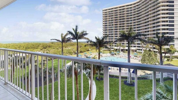 Un hotel con fachada curva, una zona de piscina con sillas de descanso y palmeras.