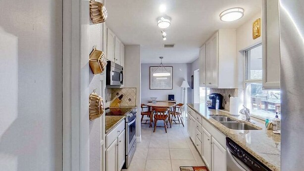 A narrow kitchen with white cabinets, a dining table, and a coffee maker. - Dog-Friendly, Snowbird-Ready Florida Escape – Near Beaches & Golf (Port Charlotte)